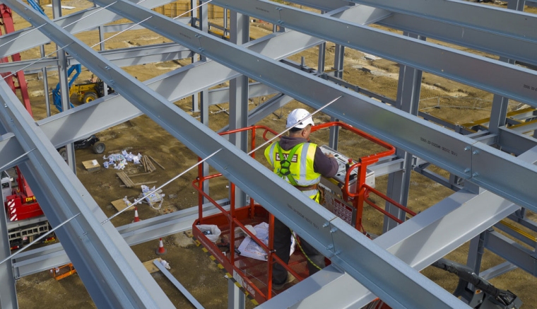 A construction worker erecting steel girders on a large construction site