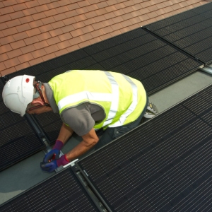 A workman fitting solar photo voltaic panels to a flat roof