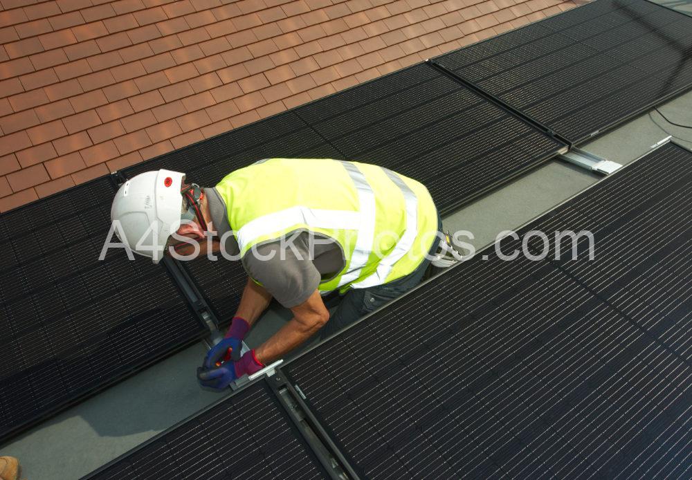 A workman fitting solar photo voltaic panels to a flat roof