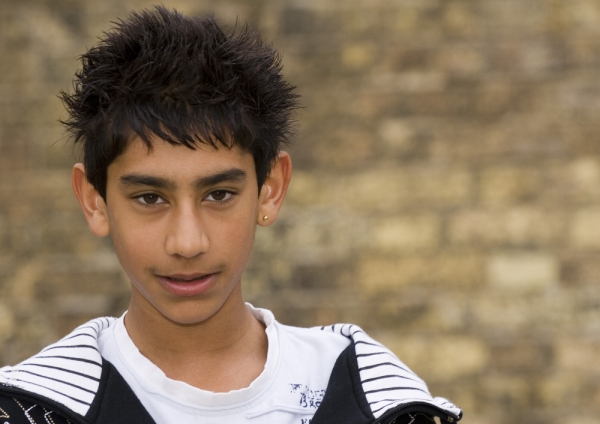 A young mixed race boy standing in front of a wall in an urban setting