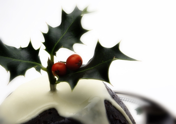 A Christmas pudding with cream and a sprig of holly on top