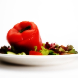 A stuffed red pepper with a green salad on a white plate