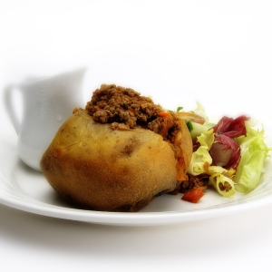 A baked potato stuffed with minced beef with green salad and gravy