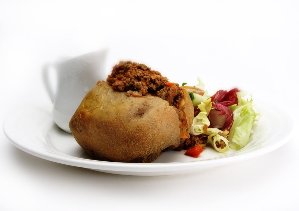 A baked potato stuffed with beef mince with a green salad and gravy