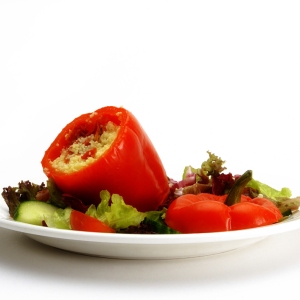 A stuffed red pepper with a green salad on a white plate