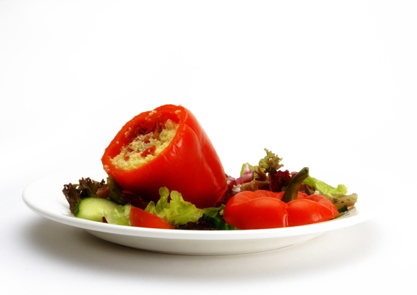 A stuffed red pepper with a green salad on a white plate