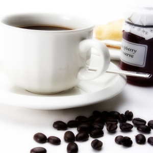 A cup of coffee with some arabica coffee beans, jam and doughnut