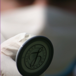 A macro view of a stethoscope held by a doctor or nurse wearing mask, gloves and scrubs