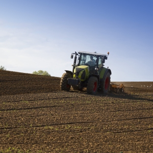 A green tractor towing an orange cultivator to lightly cultivate and turn an arable field in preparation for the sowing of a winter wheat or barley crop