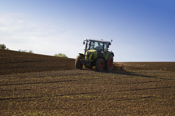 A green tractor towing an orange cultivator to lightly cultivate and turn an arable field in preparation for the sowing of a winter wheat or barley crop