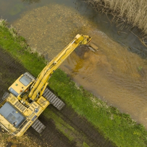 A large tracked digger placing stone & gravel into a river to raise the riverbed