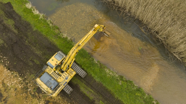 A large tracked digger placing stone & gravel into a river to raise the riverbed