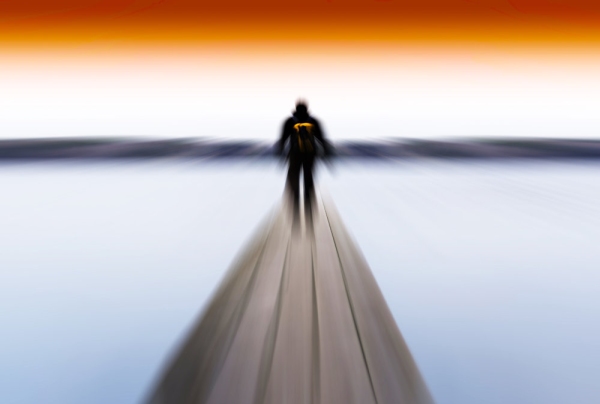 Blurred image of a man walking on a wooden jetty on a lake or sea