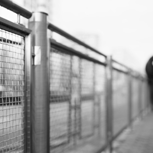 A blurred image of a man leaning against a metal fence in an urban setting