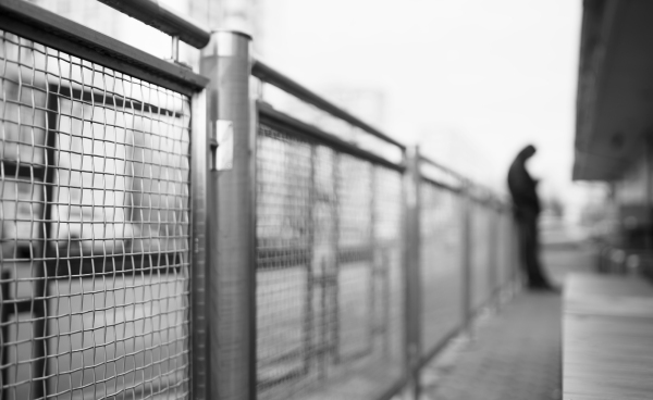 A blurred image of a man leaning against a metal fence in an urban setting