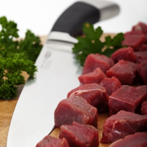 Chopped braising steak on a chopping board with carving knife. Out of focus background