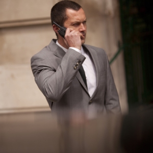 A close protection security officer on the radio to HQ or colleagues on a job in front of a limo waiting for important clients to emerge from a building