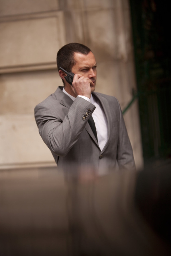 A close protection security officer on the radio to HQ or colleagues on a job in front of a limo waiting for important clients to emerge from a building