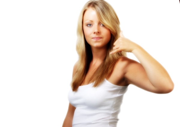 Blonde girl in white looking at camera and making phone gesture