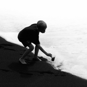 A boy playing in the surf on a black beach