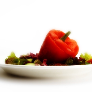 A stuffed red pepper with a green salad on a white plate