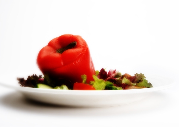 A stuffed red pepper with a green salad on a white plate