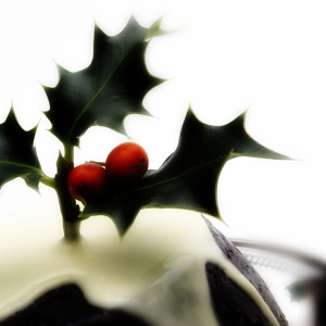 A Christmas pudding with cream and a sprig of holly on top