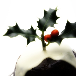 A Christmas pudding with cream and a sprig of holly on top