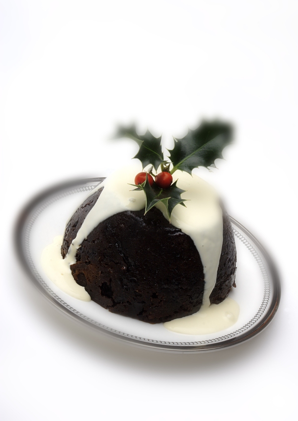 A Christmas pudding with cream and a sprig of holly on top