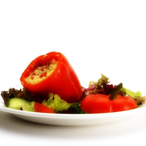 A stuffed red pepper with a green salad on a white plate