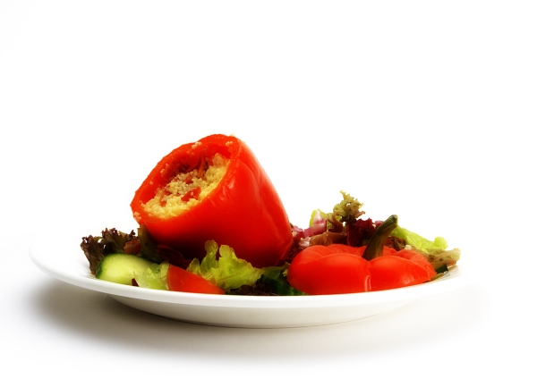 A stuffed red pepper with a green salad on a white plate