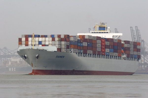 A giant container ship leaving port, stacked high with containers.