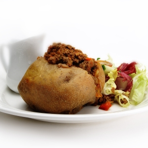 A baked potato stuffed with beef mince with a green salad and gravy