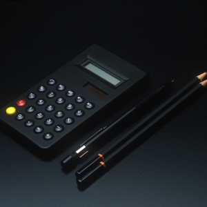 A dark and moody image of a stylish calculator and black pencils