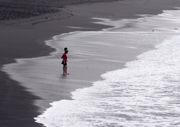 Holidaymaker wading in the surf on a black beach in Tenerife