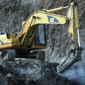 A large digger breaking rocks on a mountainside