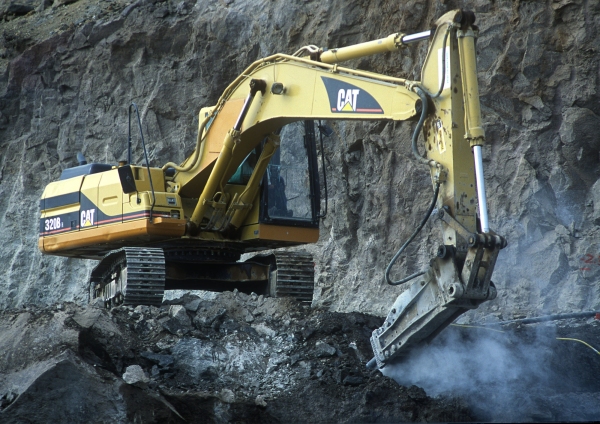 A large digger breaking rocks on a mountainside