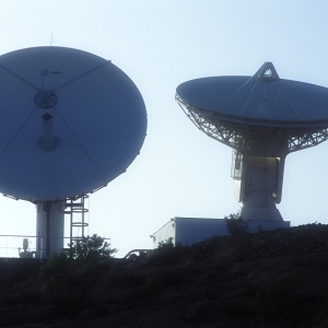 Two satellite dishes silhouetted on a remote hilltop