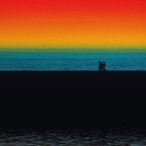 A group of walkers walking on the shoreline with wild colours in the sky