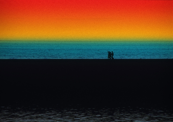 A group of walkers walking on the shoreline with wild colours in the sky