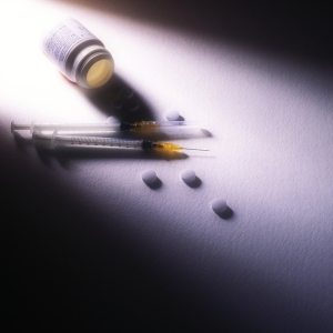 A dramatically lit image of pills and syringes