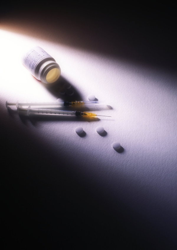 A dramatically lit image of pills and syringes