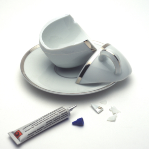 An image of an expensive but broken cup and saucer with a tube of superglue