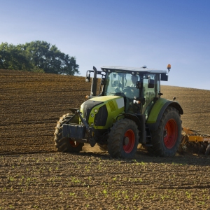 A green tractor towing an orange cultivator to lightly cultivate and turn an arable field in preparation for the sowing of a winter wheat or barley crop