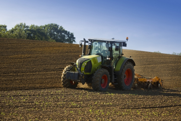 A green tractor towing an orange cultivator to lightly cultivate and turn an arable field in preparation for the sowing of a winter wheat or barley crop