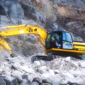 A large 360 digger breaking down a rocky clifftop to build a road