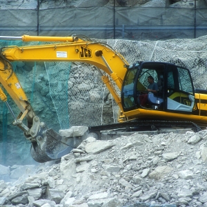 A large 360 digger with caterpillar tracks breaking rocks on a mountain road construction site