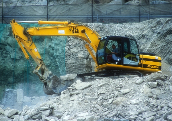 A large 360 digger with caterpillar tracks breaking rocks on a mountain road construction site