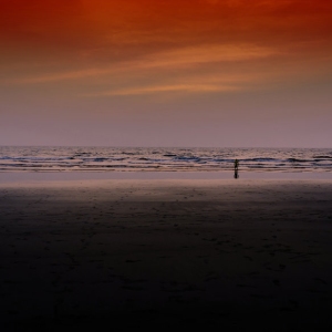 Figure wading on an empty beach in the sunset with vivid colours