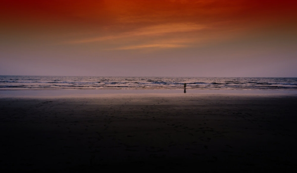 Figure wading on an empty beach in the sunset with vivid colours